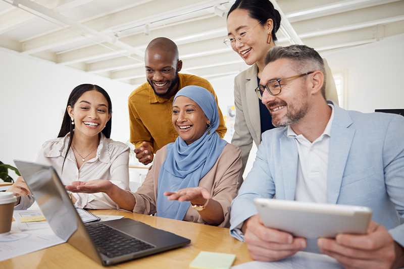 A group of five educators gathered around an open laptop.