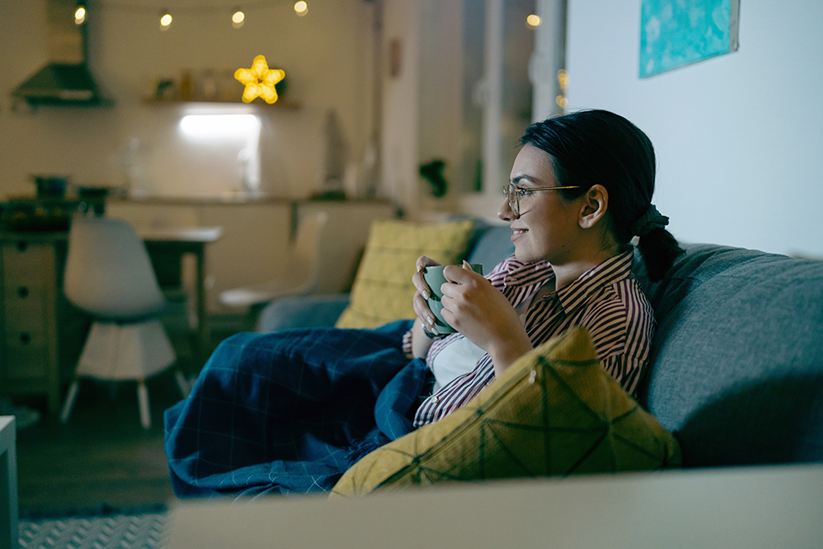 Woman watching TV on the sofa holding a mug of tea.